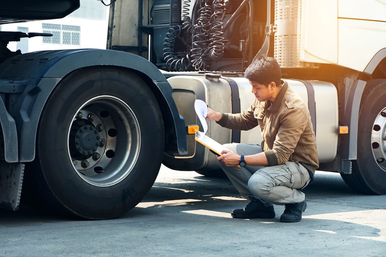 Asian truck driver holding clipboard inspecting safety a truck tires.